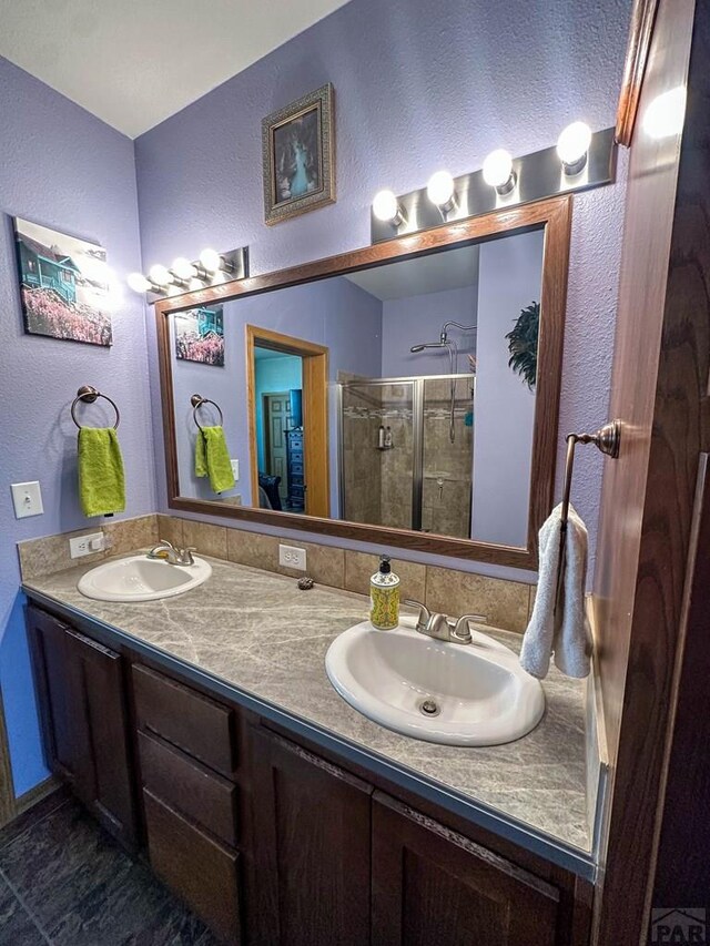 bathroom with a textured wall, double vanity, a sink, and a shower stall