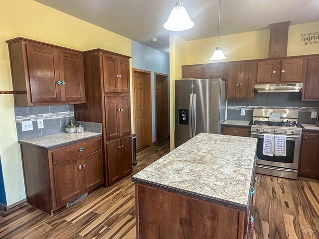 kitchen with decorative backsplash, a kitchen island, appliances with stainless steel finishes, hanging light fixtures, and under cabinet range hood