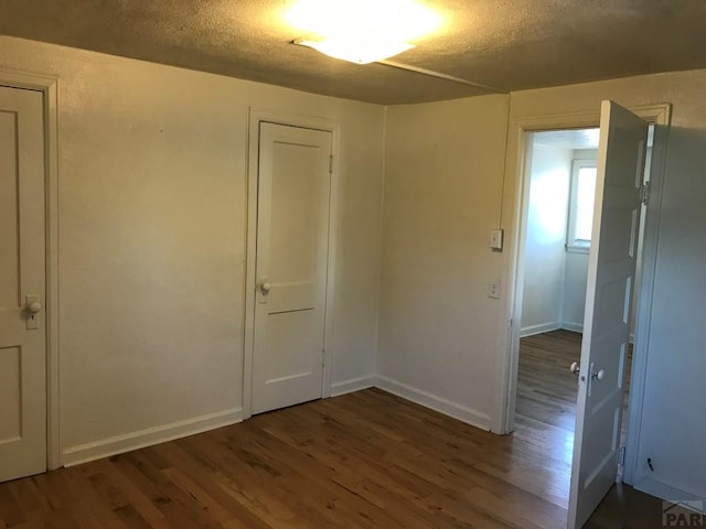 spare room with dark wood-style floors, a textured ceiling, and baseboards