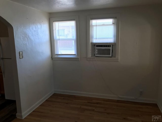 spare room with arched walkways, a textured ceiling, cooling unit, baseboards, and dark wood-style floors