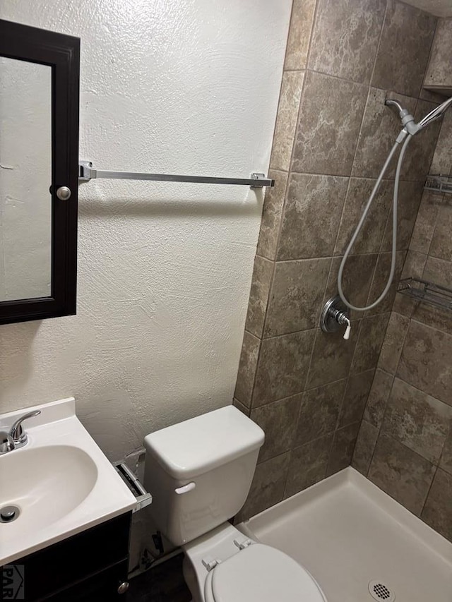 full bath with a tile shower, a textured wall, vanity, and toilet