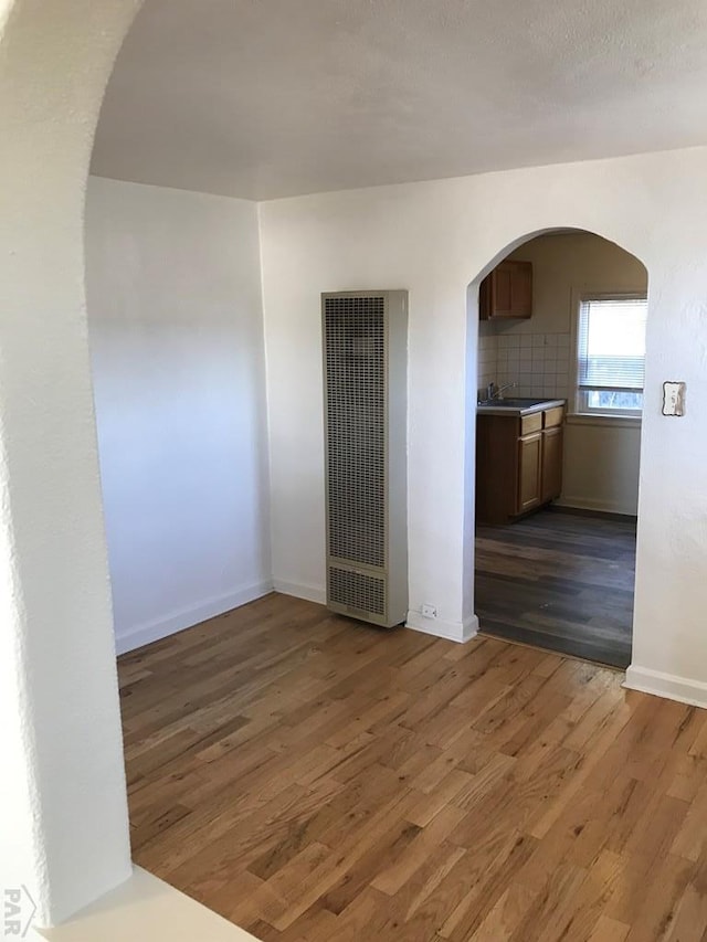 empty room featuring dark wood-style floors, arched walkways, a heating unit, a sink, and baseboards