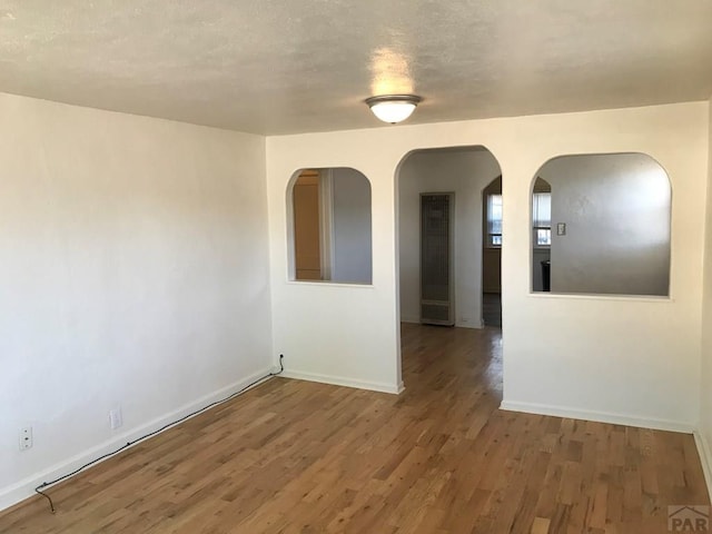 empty room featuring arched walkways, baseboards, and wood finished floors