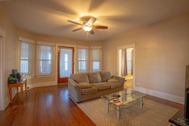 living room featuring a ceiling fan, baseboards, and wood finished floors