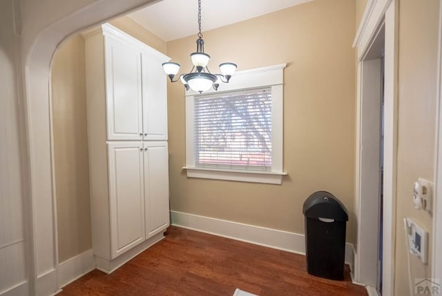 unfurnished dining area with dark wood-style flooring, a notable chandelier, and baseboards