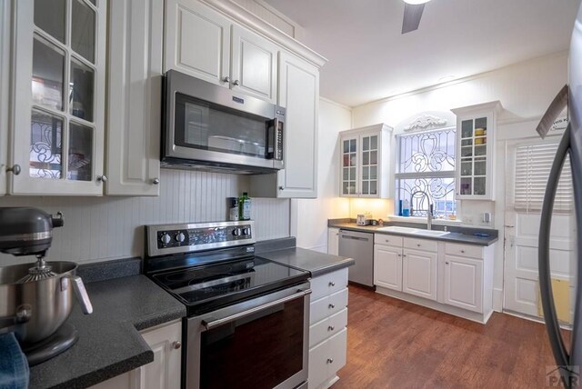 kitchen featuring dark countertops, appliances with stainless steel finishes, glass insert cabinets, white cabinetry, and a sink