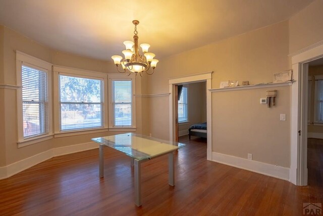 unfurnished dining area featuring dark wood-style floors, baseboards, and a chandelier