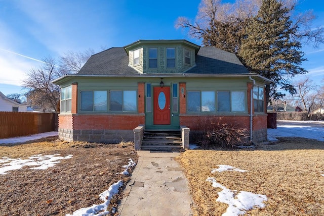 bungalow-style home with entry steps, brick siding, and fence