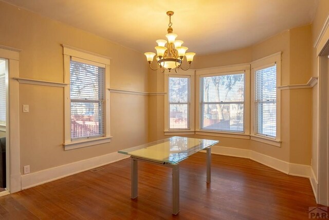 unfurnished dining area featuring a notable chandelier, visible vents, baseboards, and dark wood-style flooring