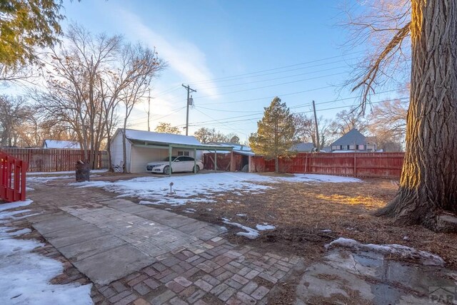 yard layered in snow featuring a carport and a fenced backyard