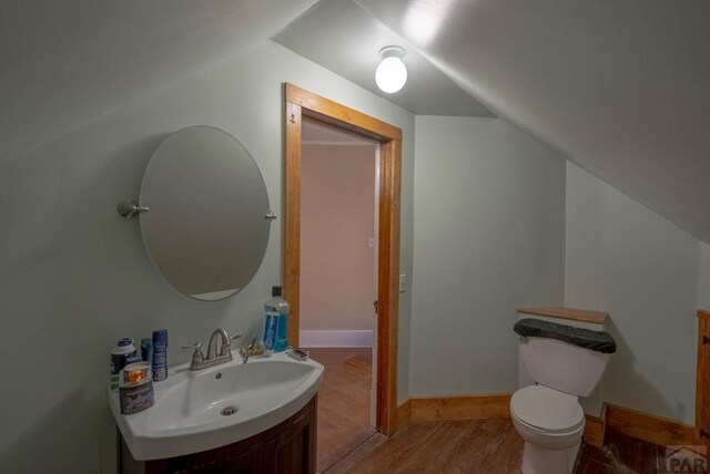 half bath featuring baseboards, toilet, wood finished floors, vaulted ceiling, and vanity