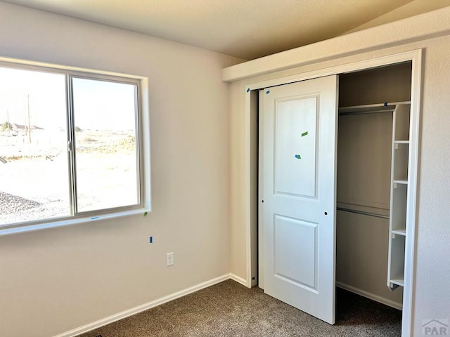 unfurnished bedroom featuring dark colored carpet, a closet, and baseboards