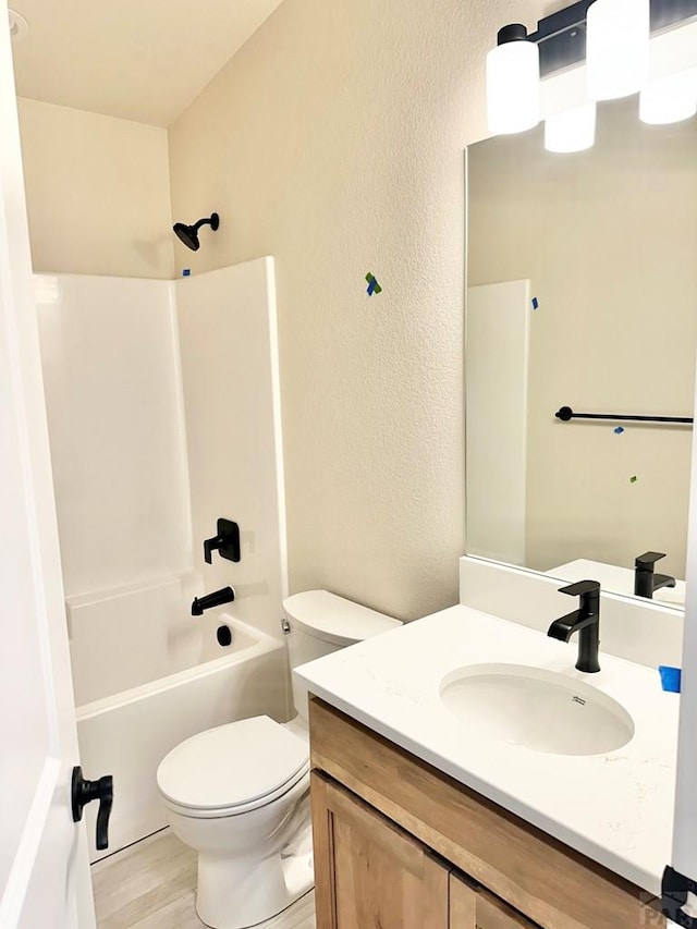 bathroom with a textured wall, toilet, wood finished floors, bathing tub / shower combination, and vanity