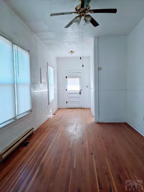 empty room with a baseboard radiator, wood finished floors, and a ceiling fan