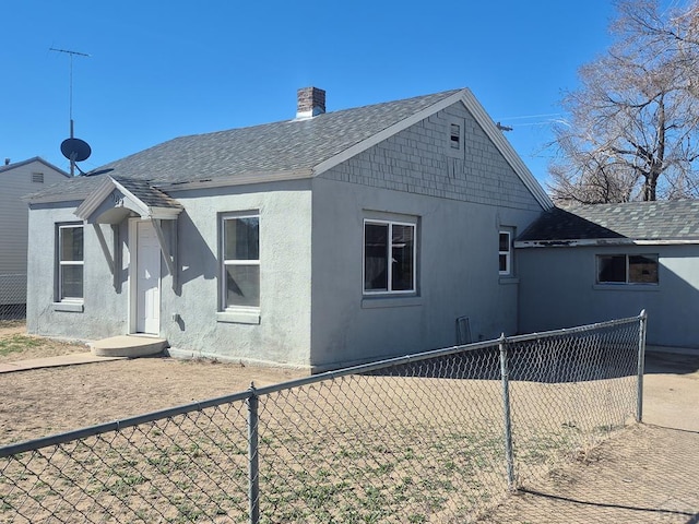 back of house featuring a shingled roof, a chimney, fence private yard, and stucco siding