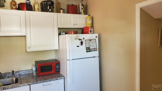 kitchen with dark countertops, white appliances, white cabinets, and a sink