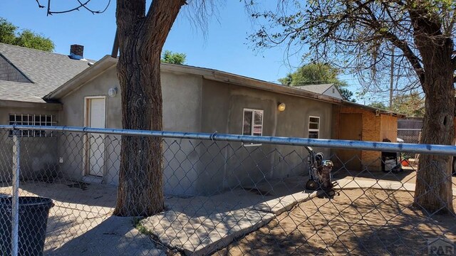 view of side of home with roof with shingles, fence, a patio, and stucco siding