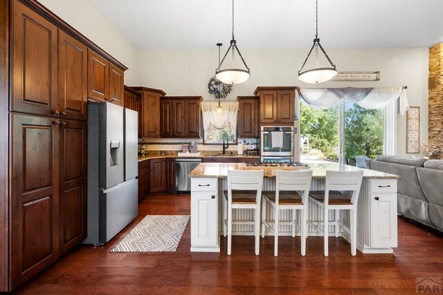 kitchen featuring appliances with stainless steel finishes, open floor plan, a kitchen breakfast bar, a center island, and hanging light fixtures