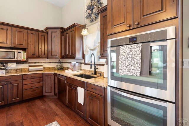 kitchen with light stone counters, stainless steel appliances, a sink, hanging light fixtures, and dark wood-style floors