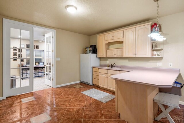 kitchen with pendant lighting, light countertops, freestanding refrigerator, a peninsula, and a kitchen breakfast bar