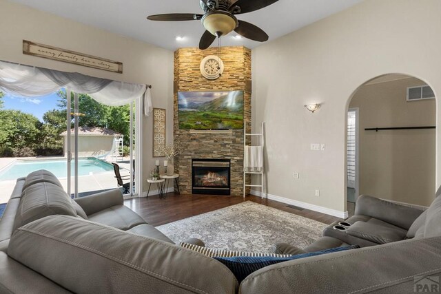 living room featuring visible vents, arched walkways, wood finished floors, and a stone fireplace