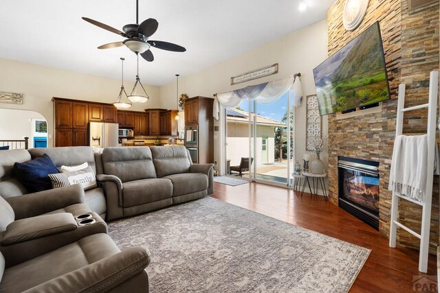 living area featuring ceiling fan, a stone fireplace, and dark wood-type flooring