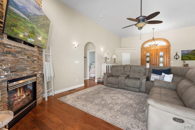 living room with arched walkways, ceiling fan, a stone fireplace, dark wood-type flooring, and baseboards