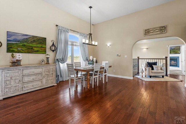 dining room with dark wood-type flooring, arched walkways, a notable chandelier, and baseboards