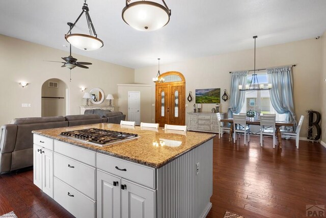 kitchen with decorative light fixtures, stainless steel gas cooktop, stone countertops, white cabinets, and a kitchen island