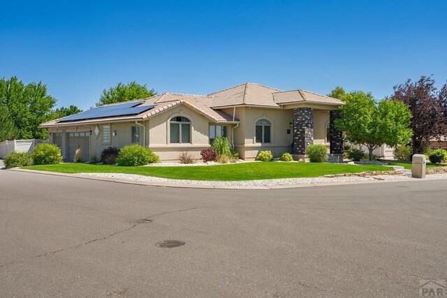 view of front of house featuring a garage, solar panels, a tiled roof, a front lawn, and stucco siding