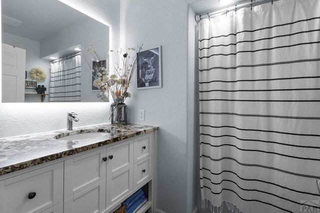 full bath featuring a textured wall and vanity