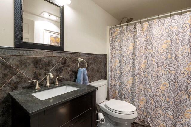 bathroom featuring wainscoting, toilet, a shower with shower curtain, vanity, and tile walls