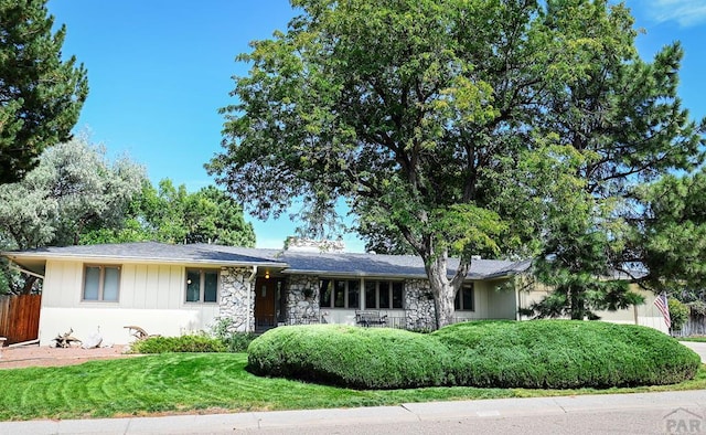 ranch-style house with a front lawn, stone siding, fence, and an attached garage