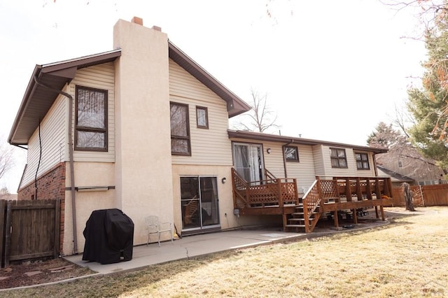 rear view of property featuring stucco siding, a deck, fence, a chimney, and a patio area