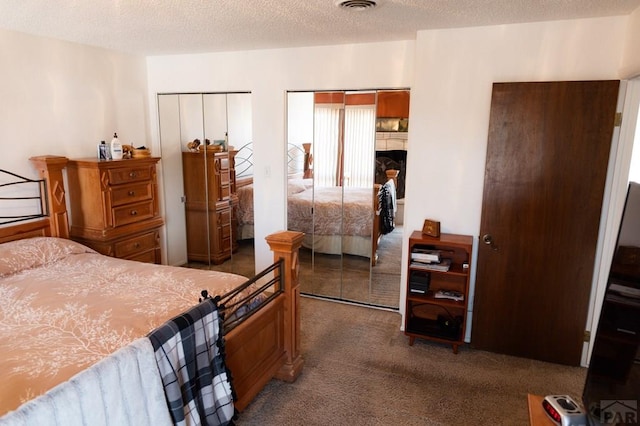 carpeted bedroom featuring visible vents, a textured ceiling, and multiple closets