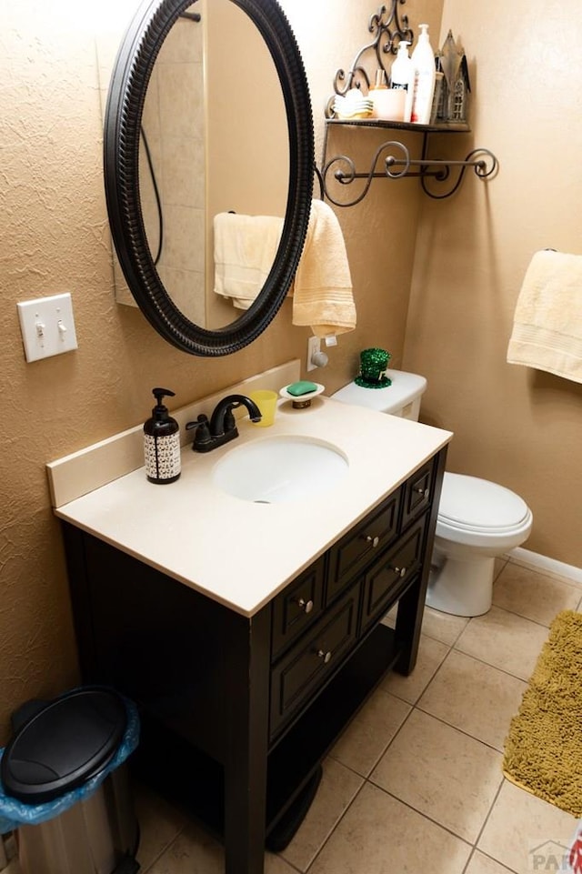 bathroom with toilet, tile patterned flooring, baseboards, vanity, and a textured wall