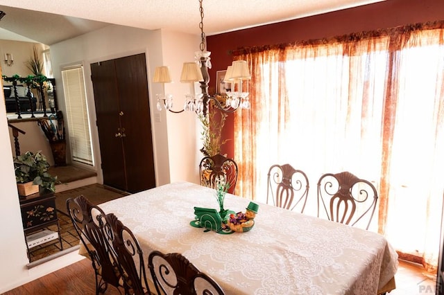 dining area with a textured ceiling, a healthy amount of sunlight, wood finished floors, and an inviting chandelier