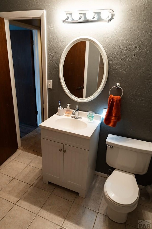 half bathroom featuring tile patterned floors, toilet, vanity, and a textured wall