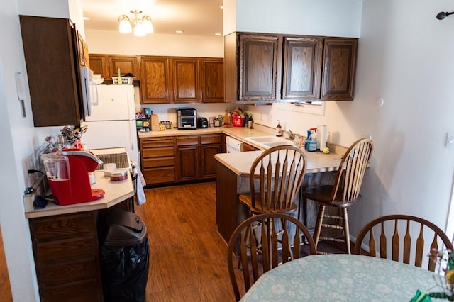 kitchen with dark wood-style floors, a peninsula, freestanding refrigerator, a sink, and light countertops