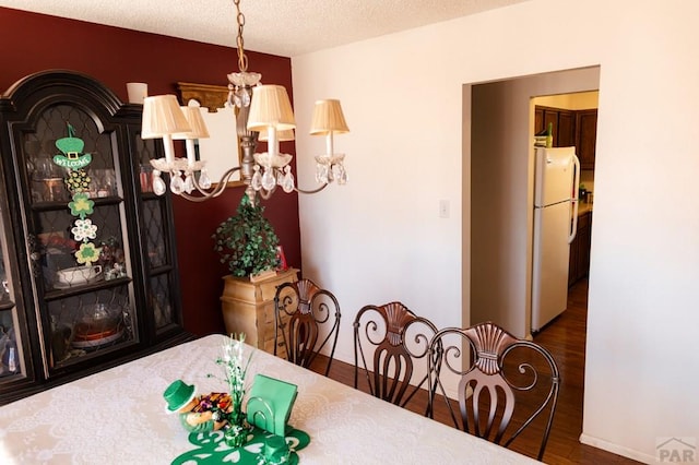 dining space featuring a notable chandelier, wood finished floors, baseboards, and a textured ceiling