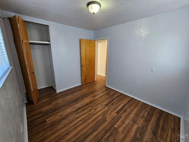 unfurnished bedroom featuring a textured ceiling, a textured wall, baseboards, a closet, and dark wood finished floors