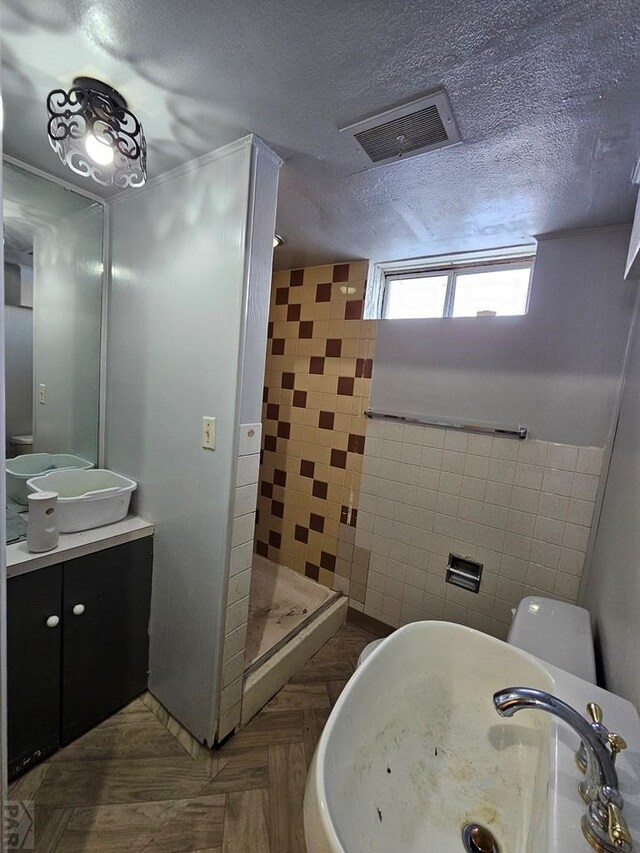 bathroom with a textured ceiling, vanity, visible vents, tile walls, and a stall shower