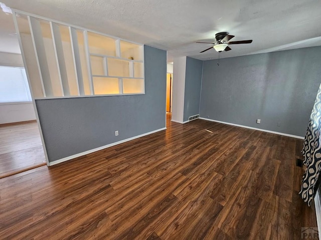 spare room featuring a ceiling fan, visible vents, baseboards, and dark wood-style flooring