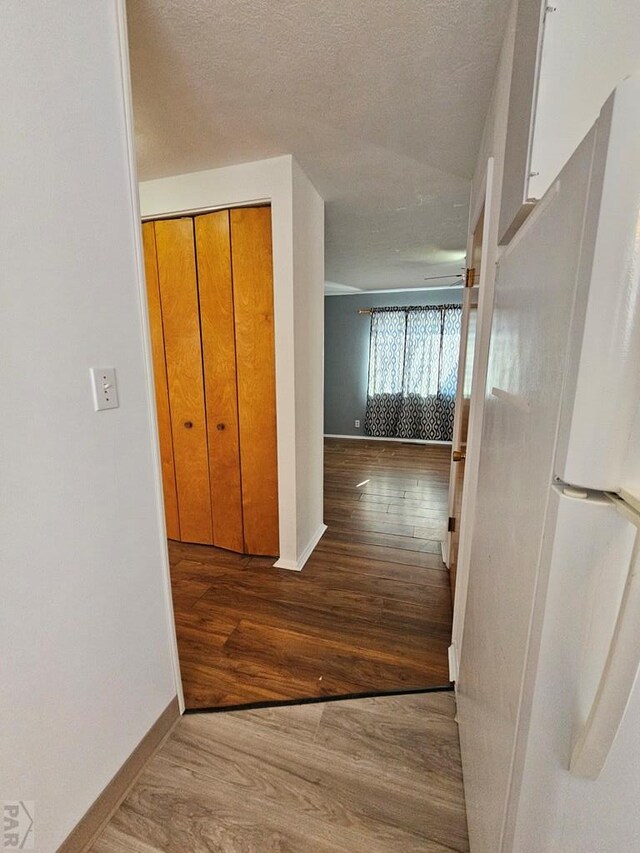 hallway with baseboards, light wood-style flooring, and a textured ceiling