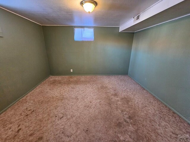 basement featuring a textured ceiling, carpet floors, visible vents, and baseboards