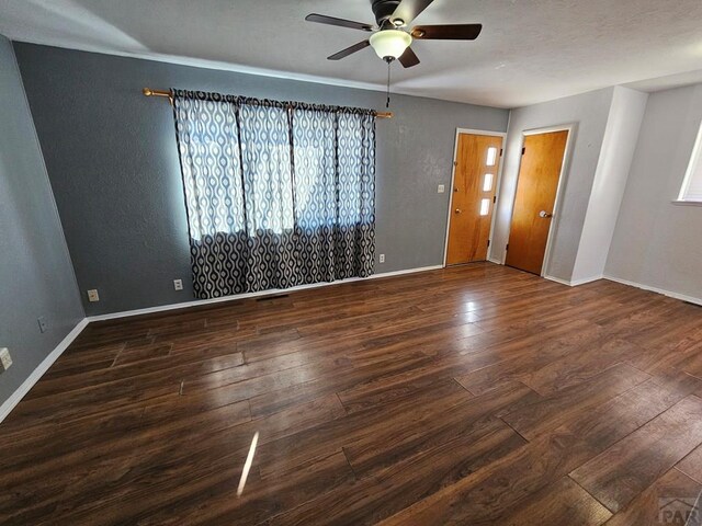 empty room featuring a ceiling fan, baseboards, and dark wood-type flooring