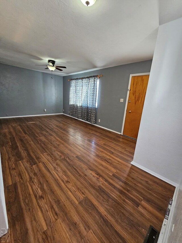 spare room featuring a textured ceiling, dark wood finished floors, and baseboards