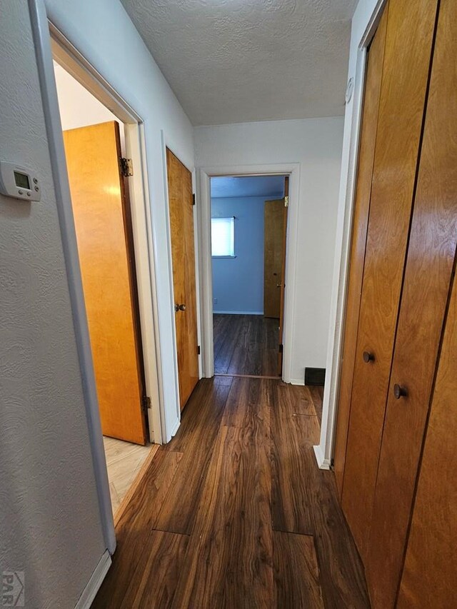 hall with a textured ceiling, dark wood-type flooring, and baseboards