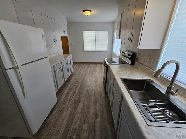 kitchen with dark wood finished floors, range with electric stovetop, light countertops, freestanding refrigerator, and a sink