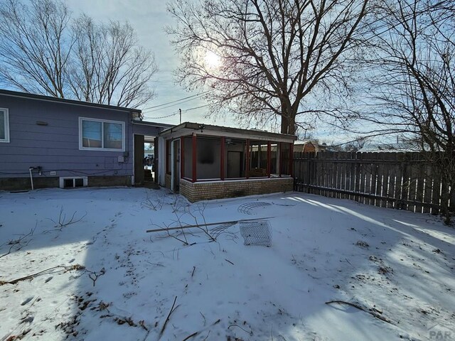 snow covered back of property with a sunroom and fence